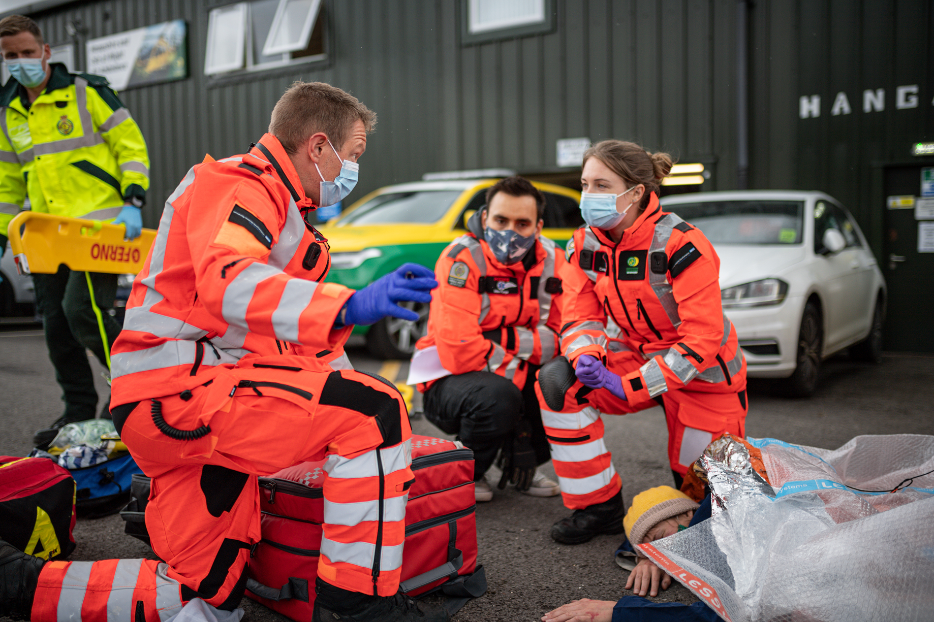 Three members of crew are taking part in an outdoor training simulation. A patient is laying on the ground.