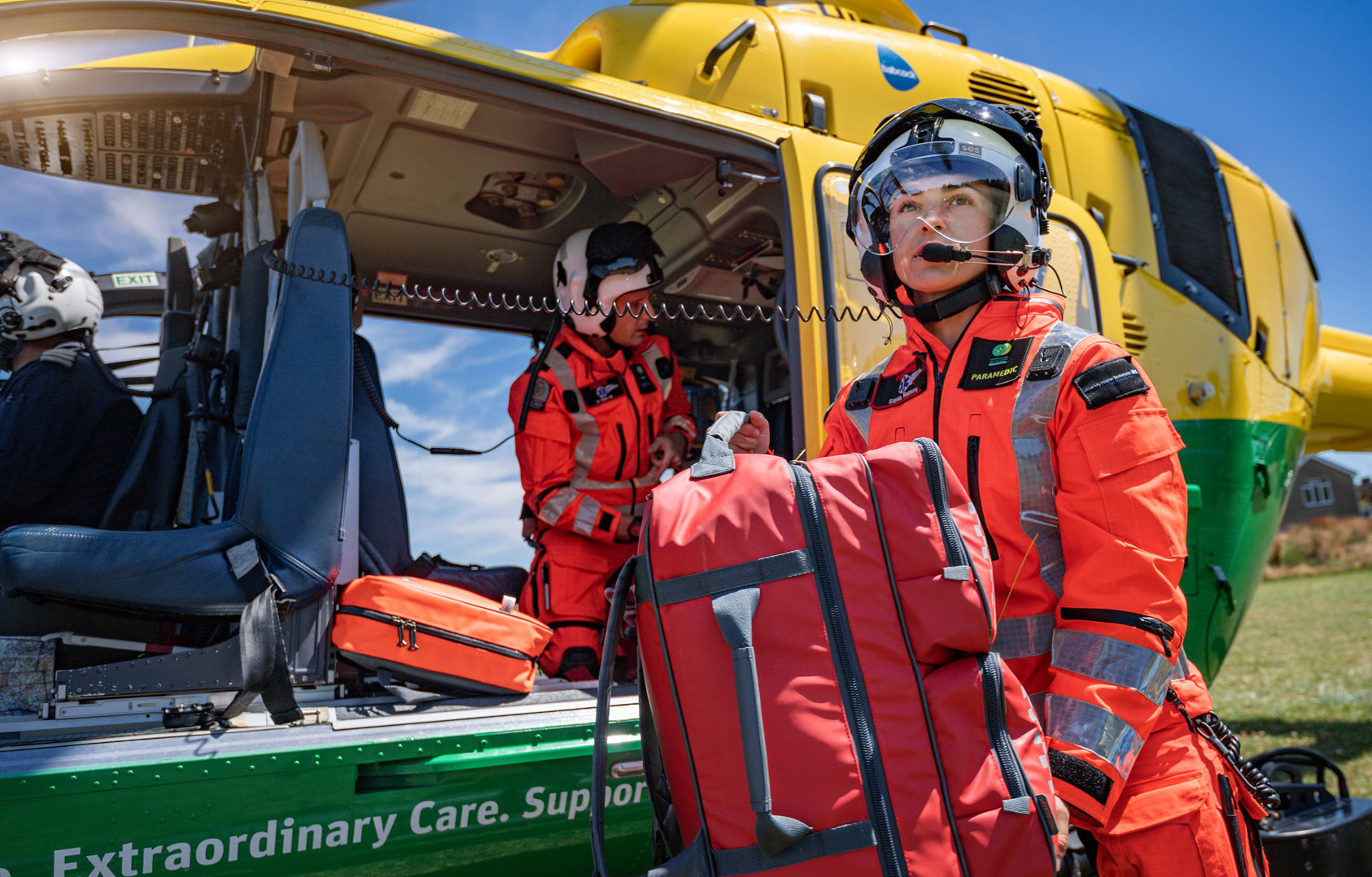 Paramedic Sophia carrying equipment out of the helicopter. Doctor Chris is inside the helicopter and the helicopter door is open.